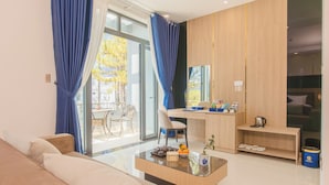 Una habitación de hotel moderna con sofá, una mesa de comedor, una pequeña cocina y un ventanal con cortinas.