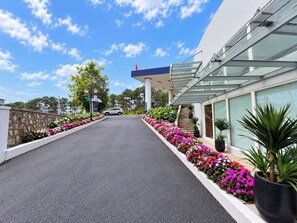 A modern building with a glass facade, a paved driveway, and a row of colorful flowers along the sides. - Tea Resort Dalat (Lac Duong)