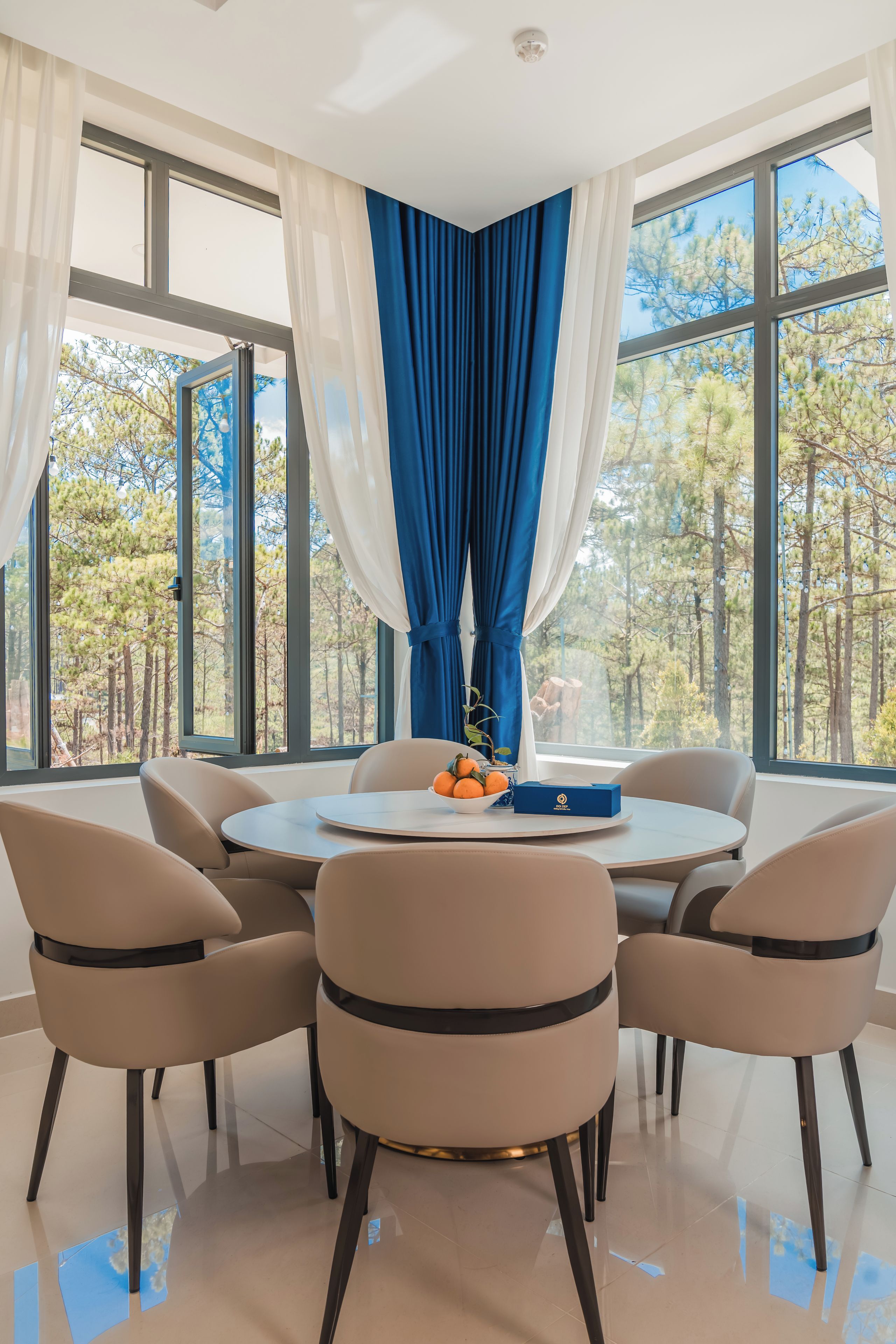 Un comedor moderno con una mesa redonda, seis sillas y vistas a un bosque a través de grandes ventanales.