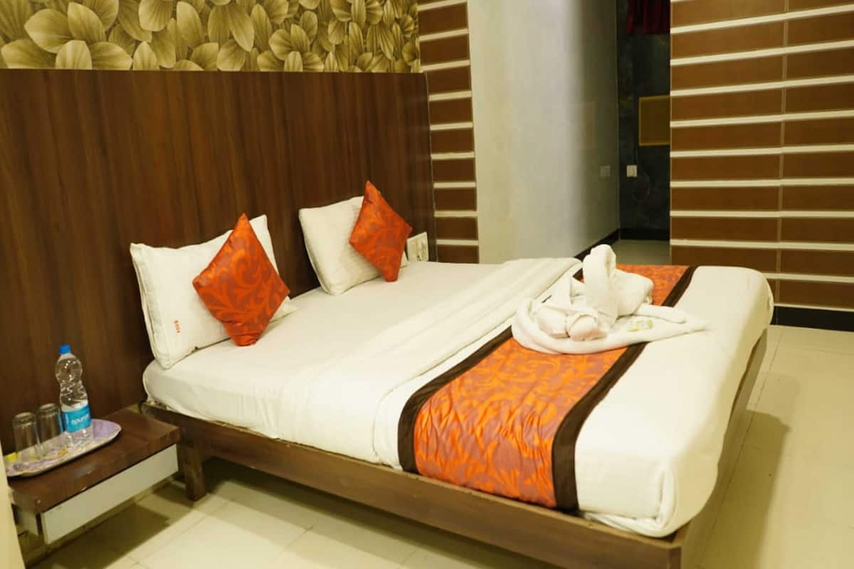 A hotel room with a wooden bed, two pillows, a water bottle, and a tray with towels.