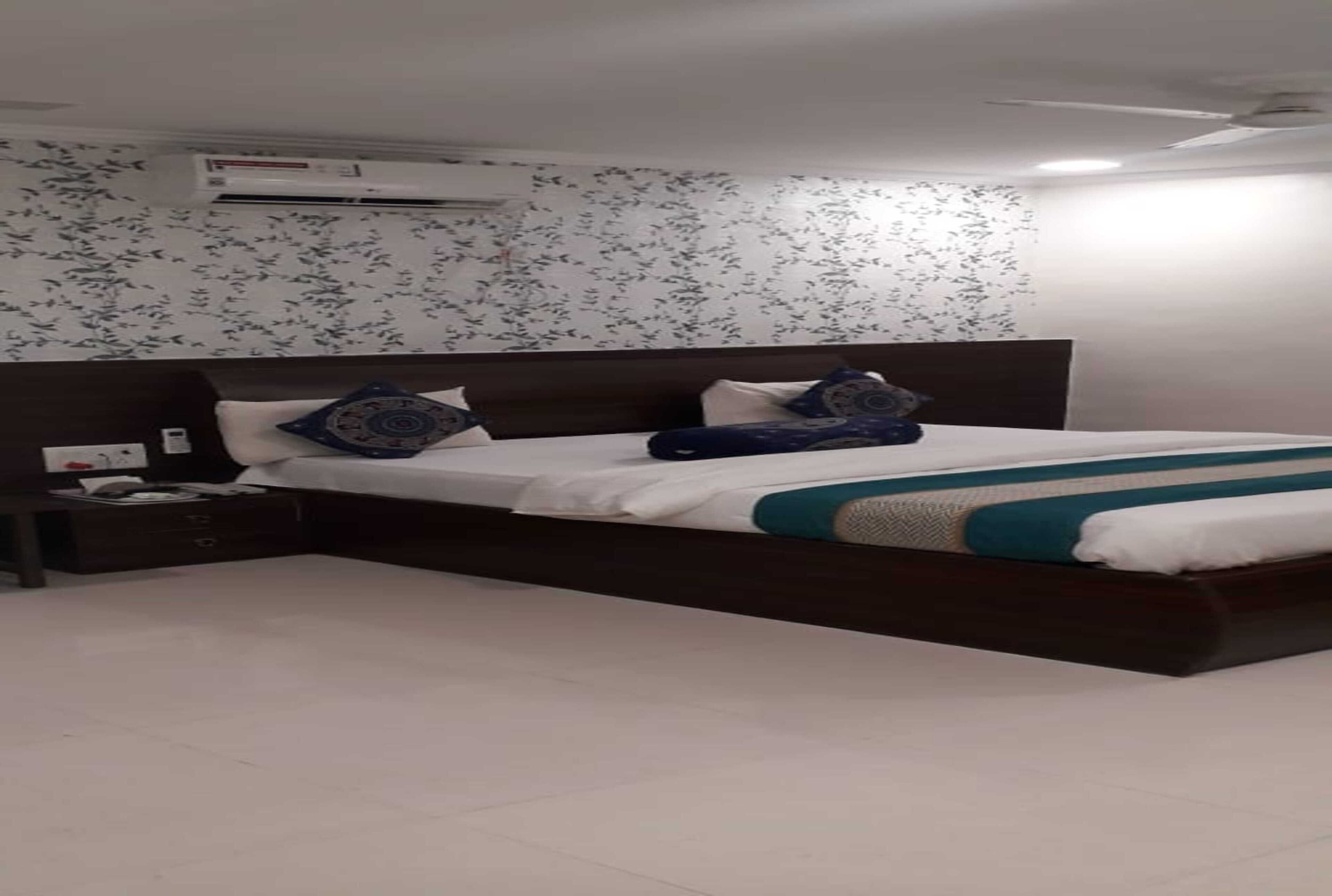 A bedroom with a bed, a nightstand, an air conditioning unit, and a wall with a floral pattern.