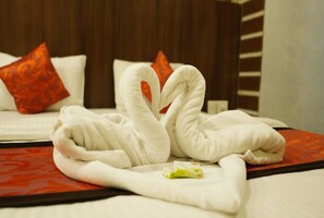 Habitación de hotel con una cama con cubrecama rojo y blanco, dos toallas blancas dispuestas en forma de corazón y una sola almohada blanca con diseño rojo.