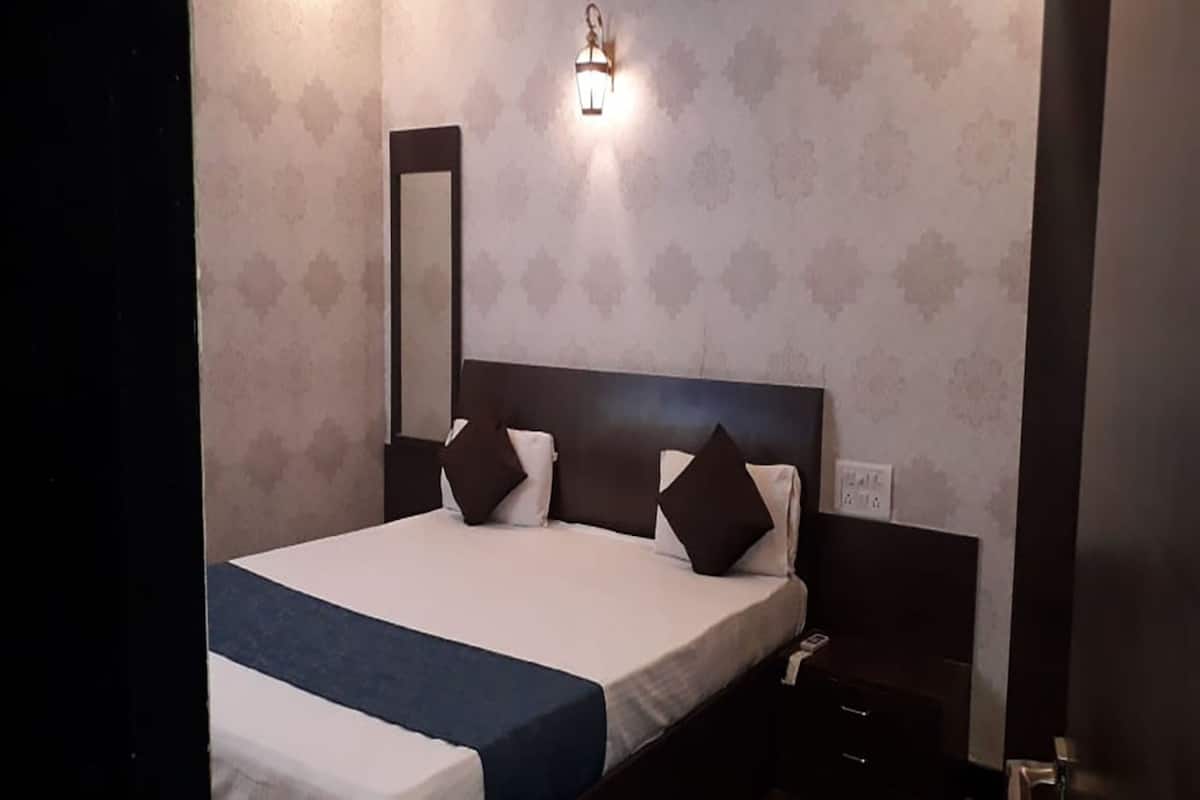 A hotel room with a large bed, a nightstand, a wall-mounted lamp, and a mirror.