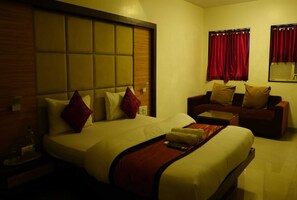 Una habitación de hotel con una cama grande, un sofá, una mesita y cortinas rojas.