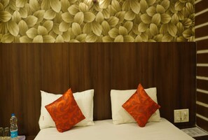 Habitación de hotel con cabecera de madera, dos almohadas con motivos anaranjados y una pared con diseño de hojas.