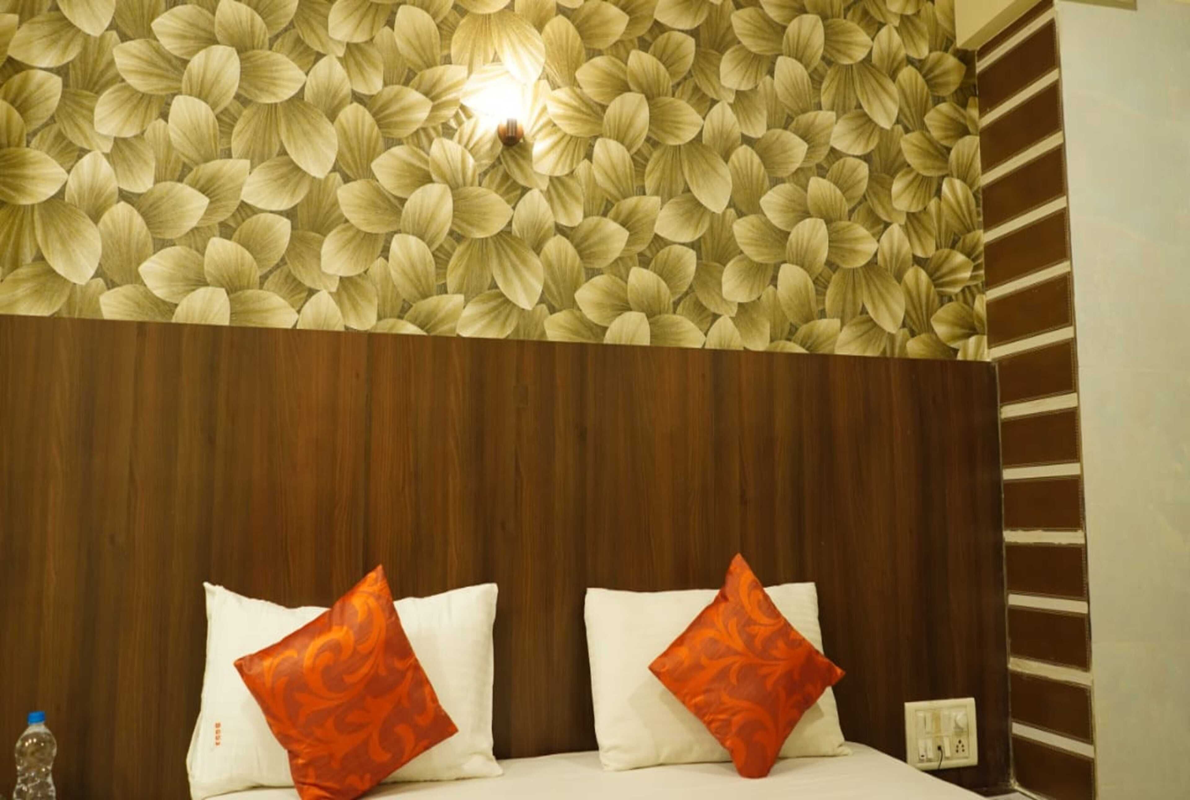 A hotel room with a wooden headboard, a floral-patterned wall, and two pillows with orange and white designs.