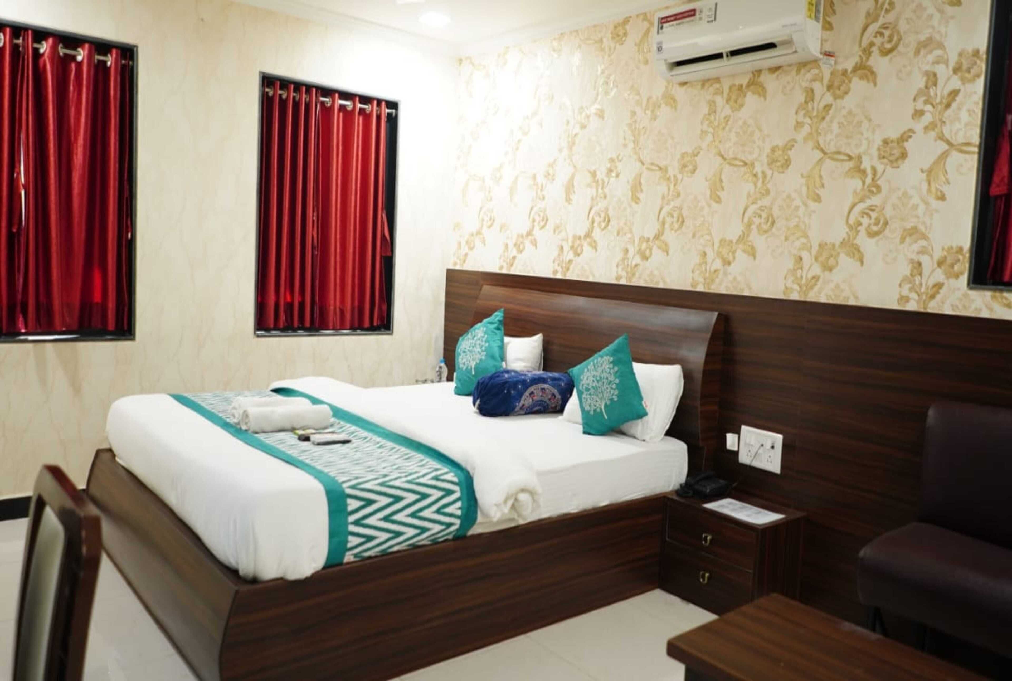 Une chambre d’hôtel avec un lit en bois, des rideaux rouges, un papier peint à motifs et une petite table de chevet.