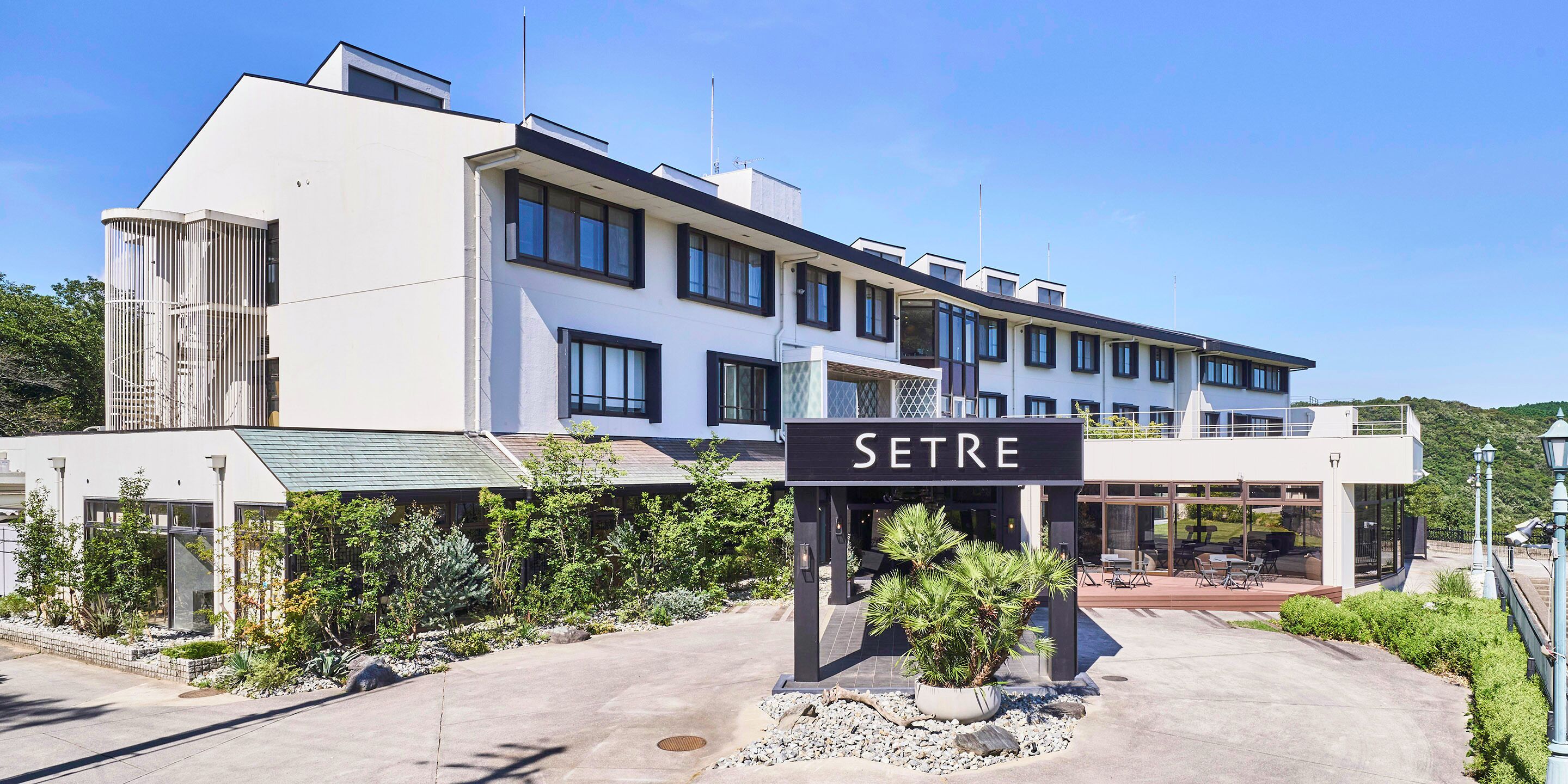 A modern hotel with a sign reading "SETRE" in front. It features a multi-story structure with large windows and a covered outdoor area with seating.
