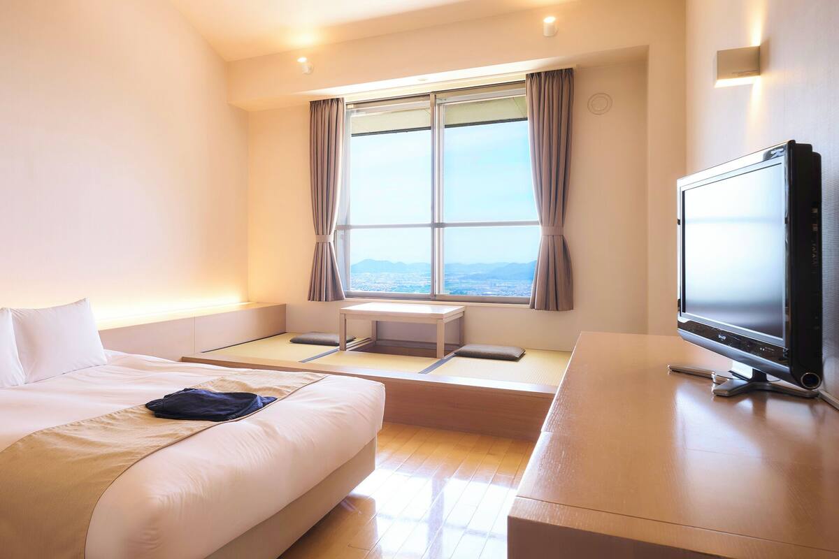 A hotel room with a bed, a desk, a television, and a window with curtains.