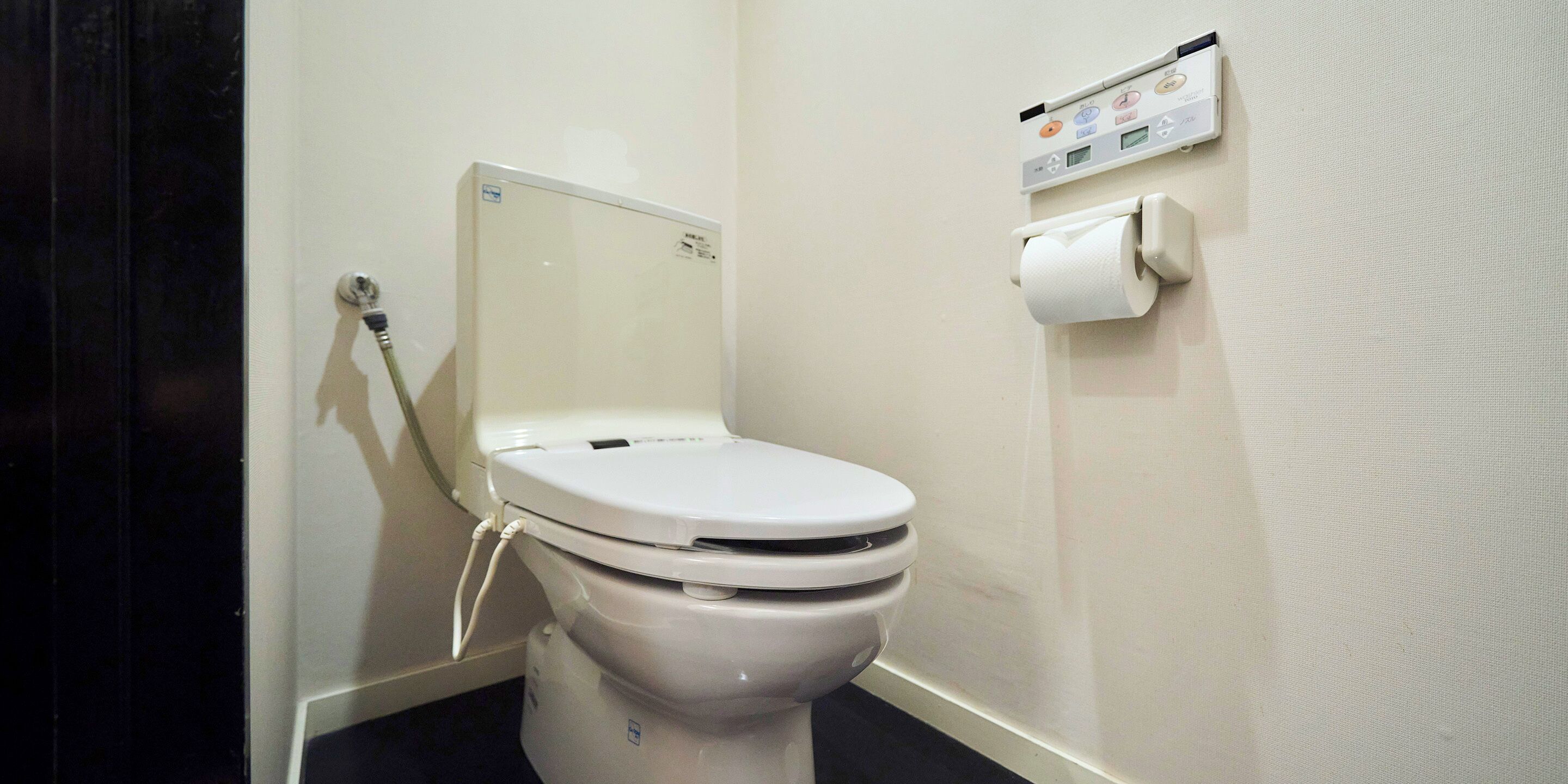 A toilet with a flush handle and a toilet paper holder on the wall.