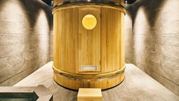 A wooden cylindrical structure with a circular window and ventilation slats, set against a tiled wall.