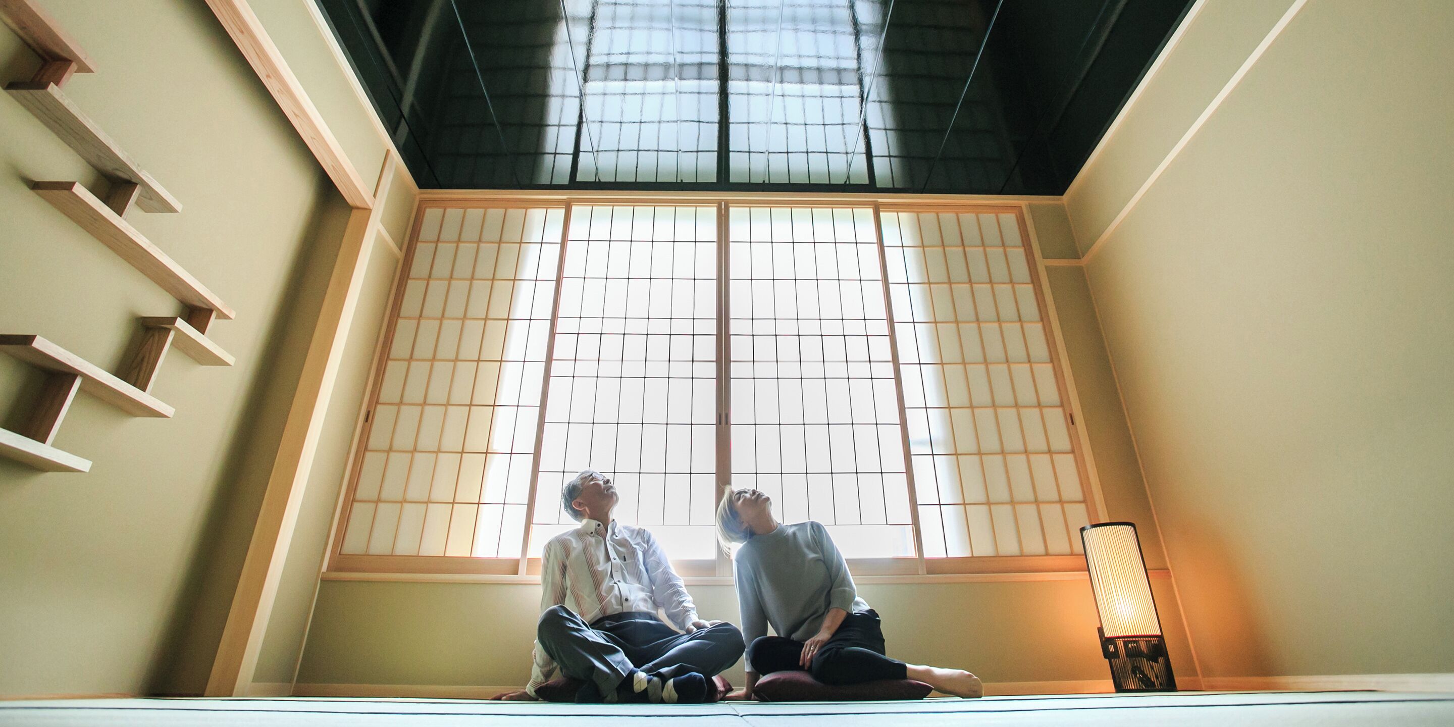 Two people sitting on tatami mats in a room with shoji screens and a traditional Japanese-style lamp.