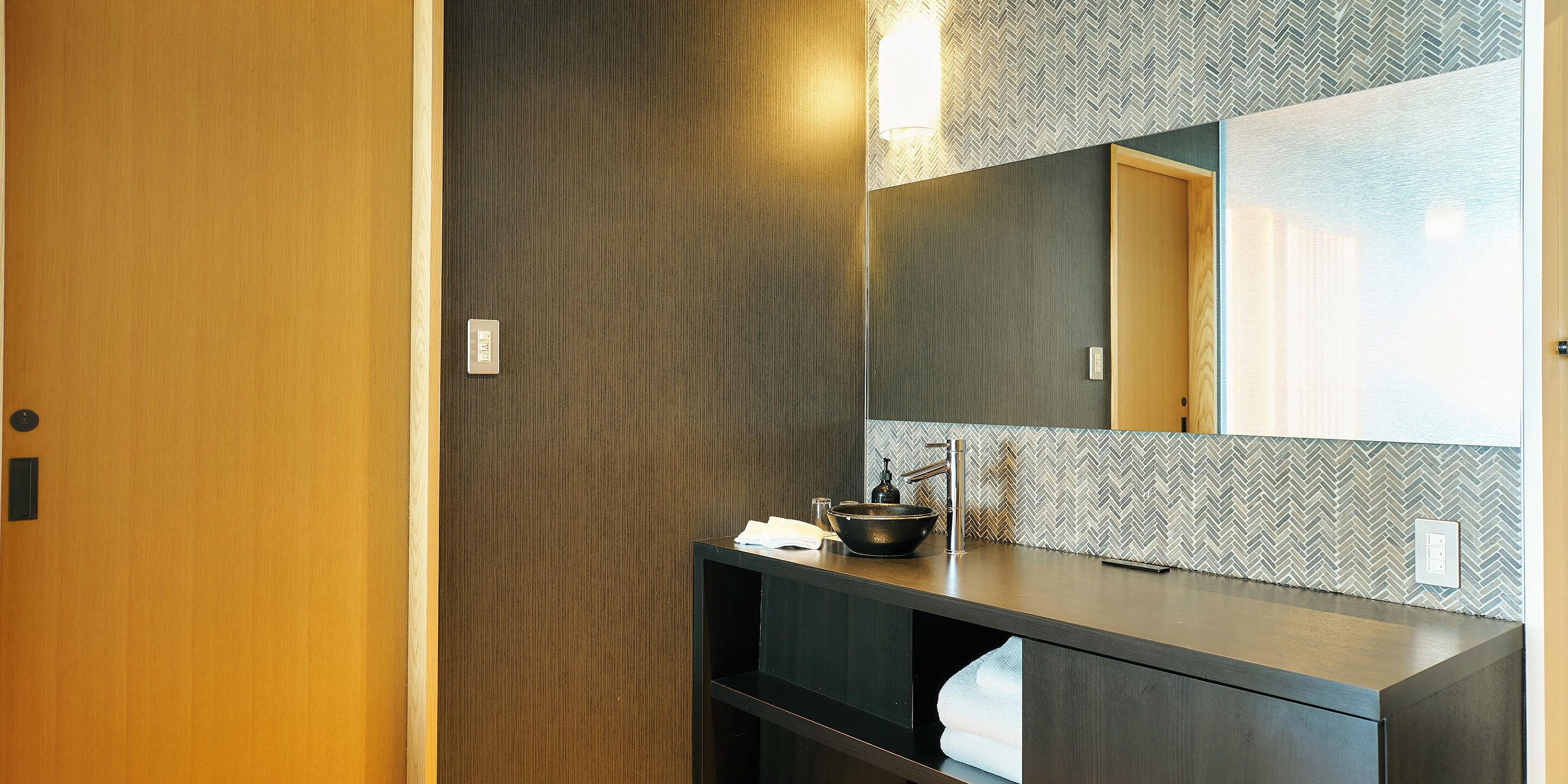 Une salle de bain moderne avec une porte en bois, un meuble-lavabo foncé, un miroir et un pare-feu en motif chevrons.