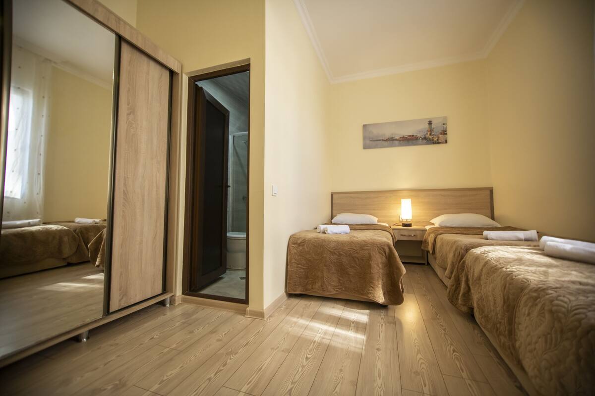 A hotel room with two beds, a wooden floor, a sliding door, and a painting on the wall.