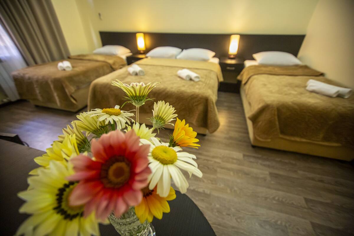 A hotel room with three single beds, each with a brown bedspread and white pillows, and a vase of flowers on the table.