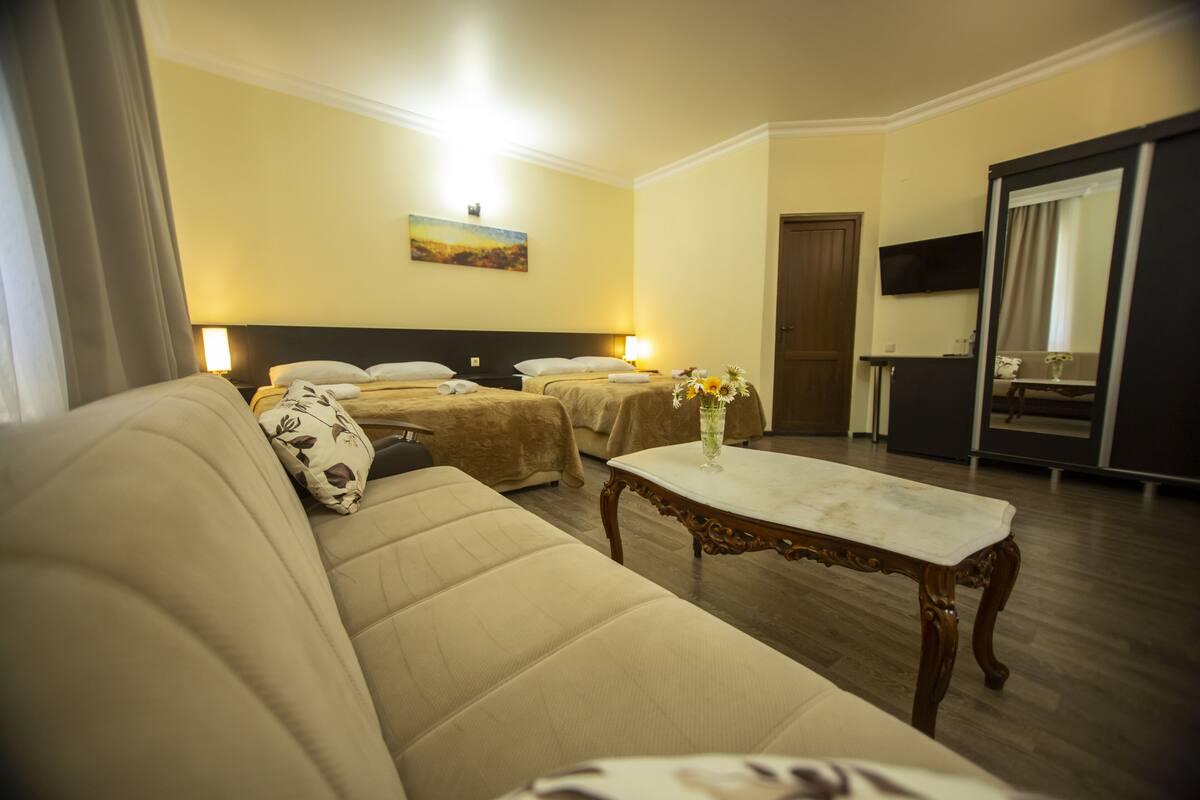 A hotel room with a sofa, two beds, a table, and a TV.
