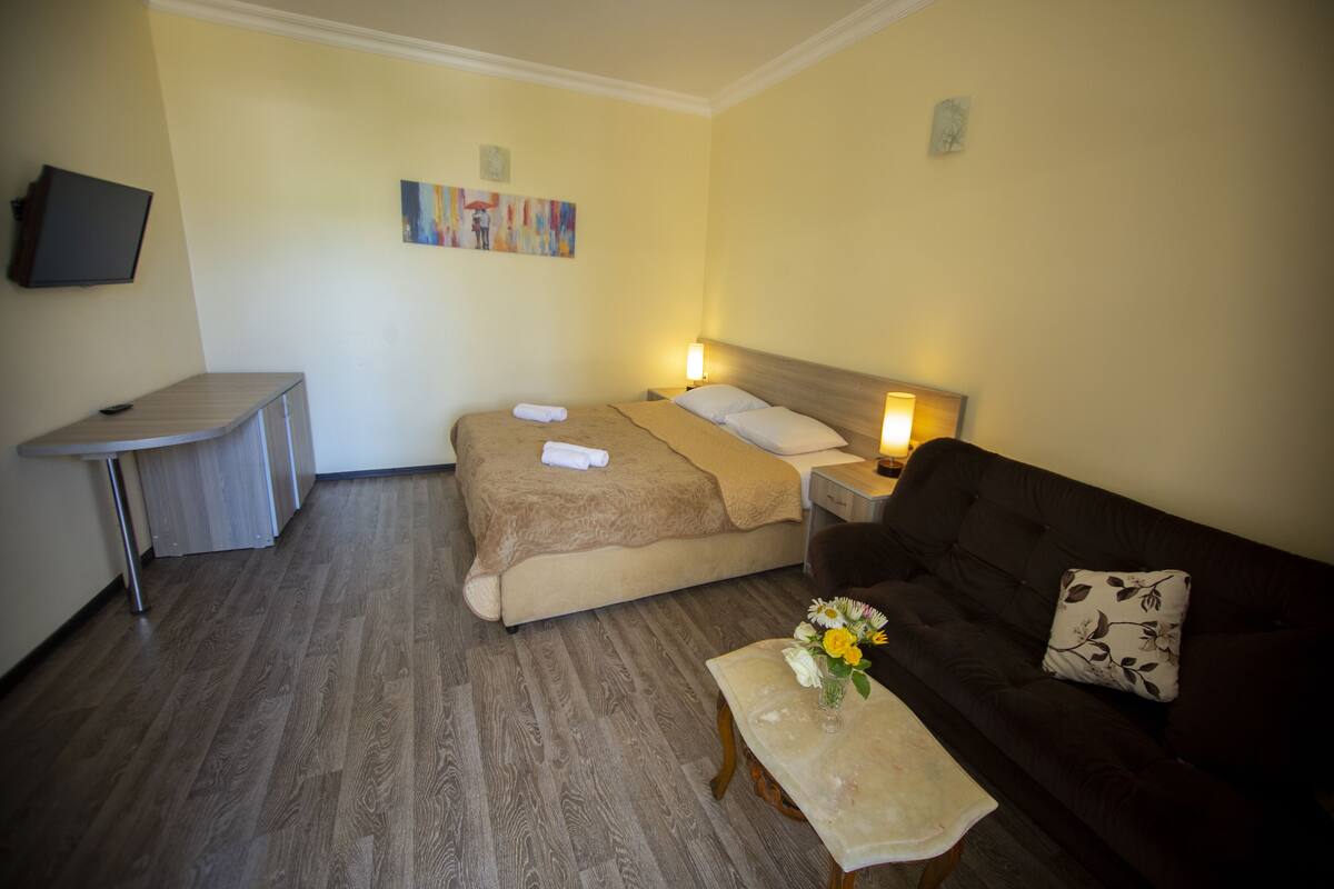 A hotel room with a bed, bedside table, lamp, sofa, and a small table with flowers.
