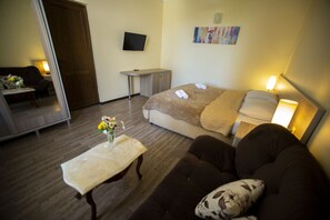 Una habitación de hotel con cama, sofá, una pequeña mesa con un florero, escritorio, televisor y un cuadro en la pared.