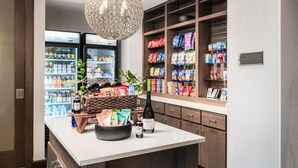 A hotel kitchen with a central island, a refrigerator stocked with beverages, and shelves with snacks. - Homewood Suites by Hilton San Jose Santa Clara (San Jose)