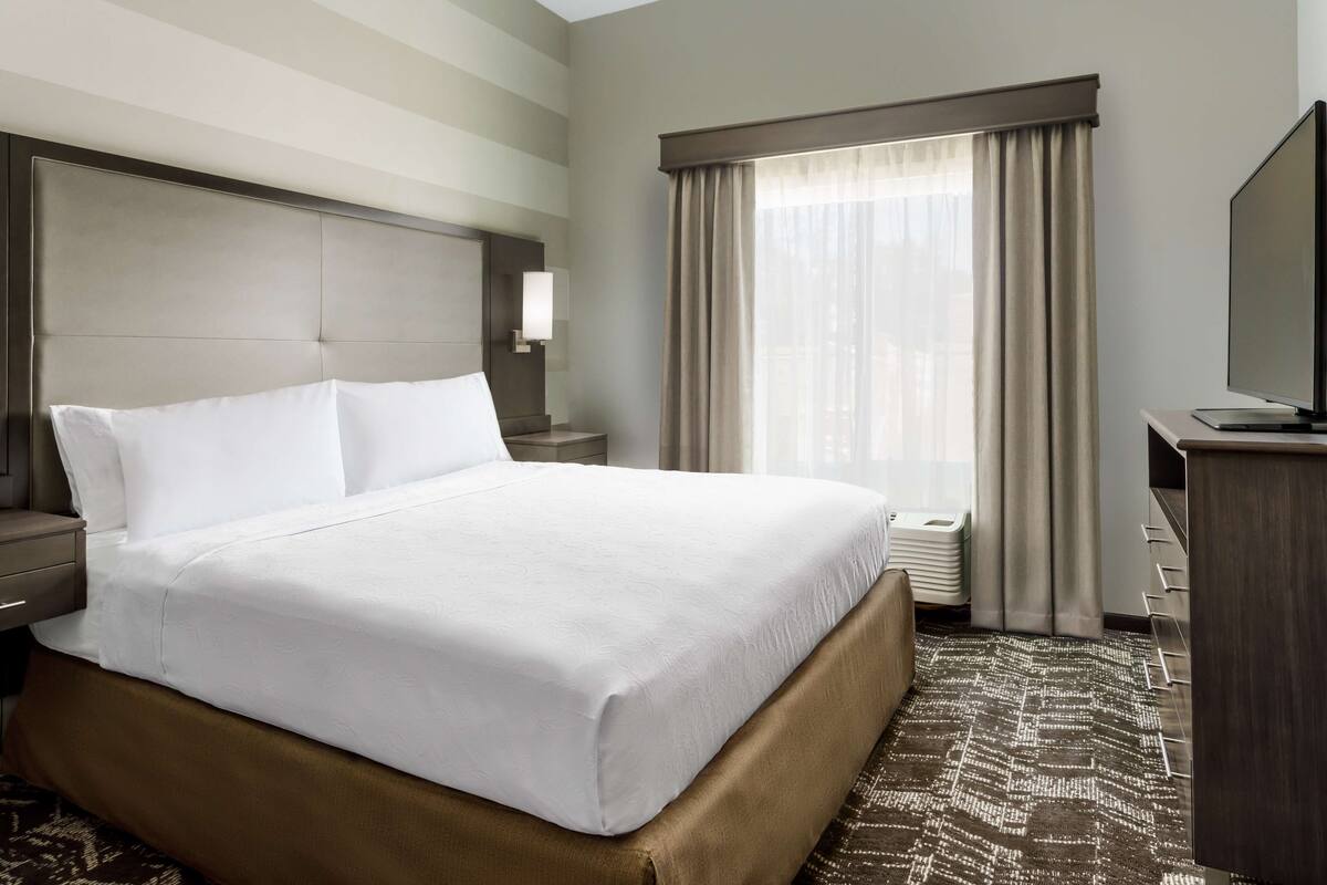 Une chambre d’hôtel avec un grand lit, un bureau, une télévision et une fenêtre avec des rideaux.