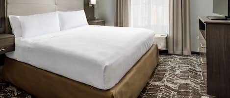 Habitación de hotel con una cama grande, un escritorio, un televisor y una ventana con cortinas.