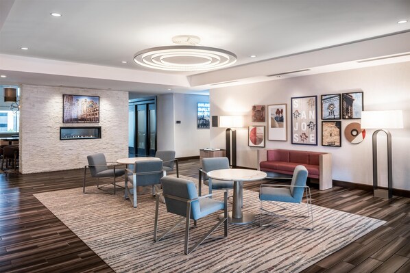 A modern hotel lobby with a stone accent wall, a seating area with round tables and chairs, and framed artwork on the walls.