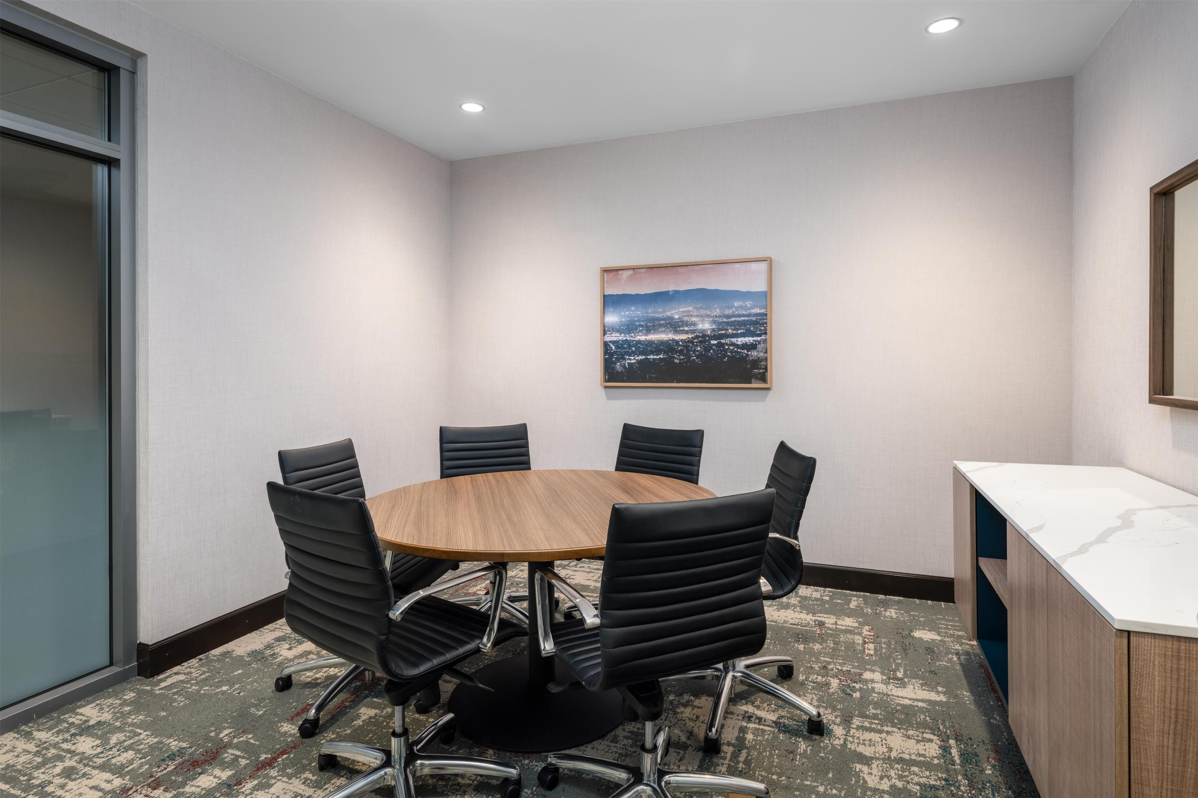 A conference room with a round table, black chairs, a whiteboard, and a cityscape painting on the wall.