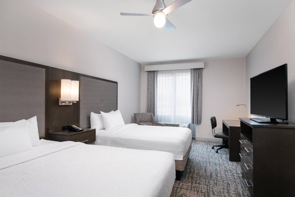 Une chambre d’hôtel avec deux lits, un bureau, une télévision et un ventilateur de plafond.