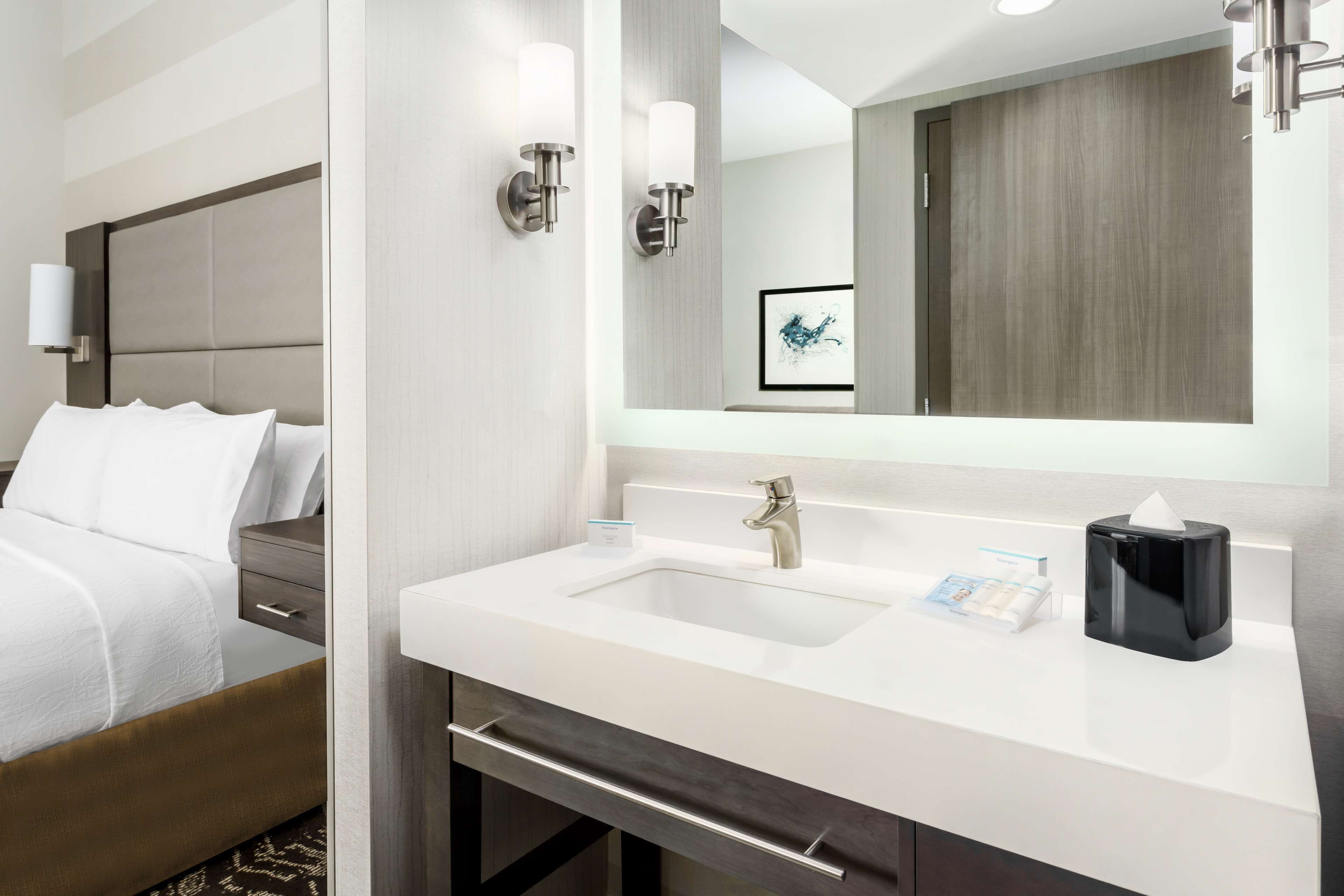 A modern hotel room with a bed, a white sink, a mirror, and a bedside table.