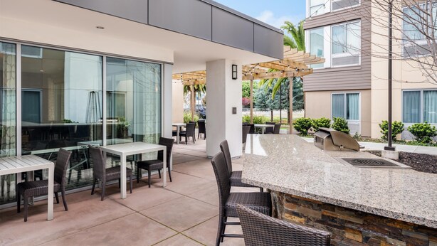 An outdoor patio area with tables and chairs, a stone countertop, and a pergola with string lights. - Homewood Suites by Hilton San Jose Santa Clara (San Jose)