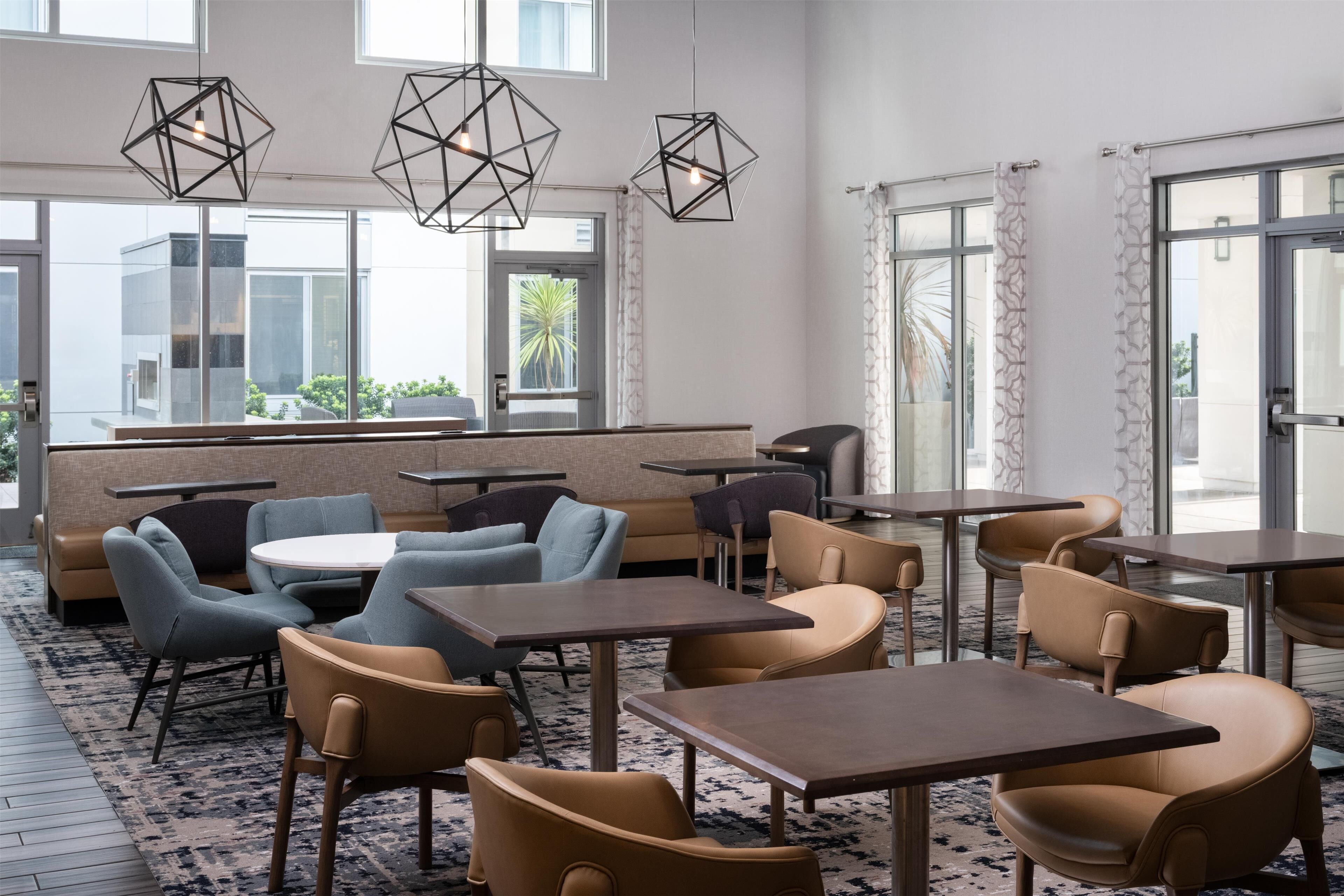 A modern dining area with geometric pendant lights, cushioned seating, and a view of the outdoors through large windows.