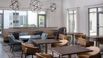Un comedor moderno con lámparas colgantes geométricas, asientos acolchados y vistas al exterior a través de amplias ventanas.