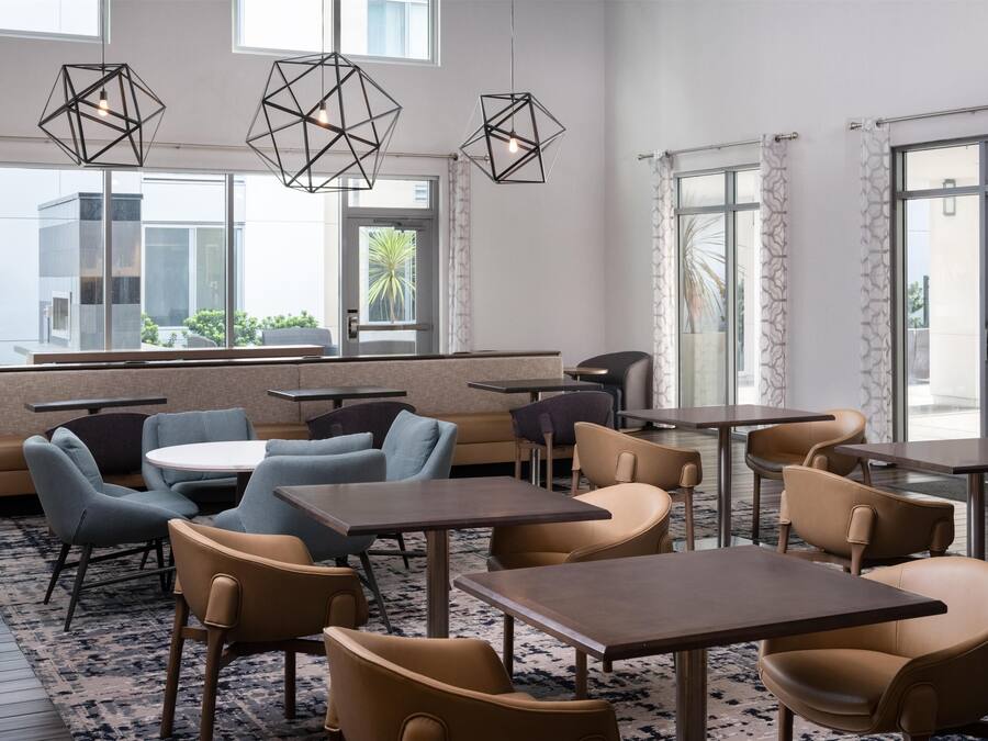 Un comedor moderno con lámparas colgantes geométricas, asientos acolchados y vistas al exterior a través de amplias ventanas.