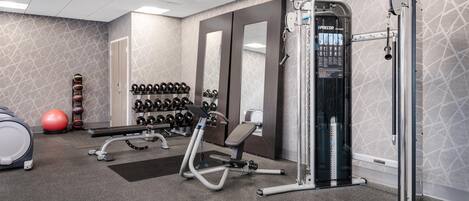 Un gimnasio con equipo de ejercicio, estantes para pesas y una cinta de correr.
