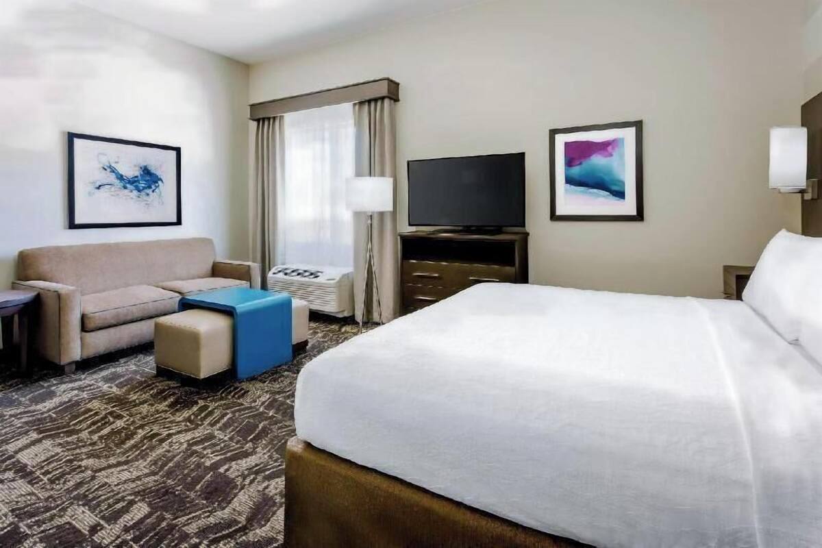 Une chambre d’hôtel avec un lit, un canapé, une télévision et des œuvres d’art accrochées aux murs.