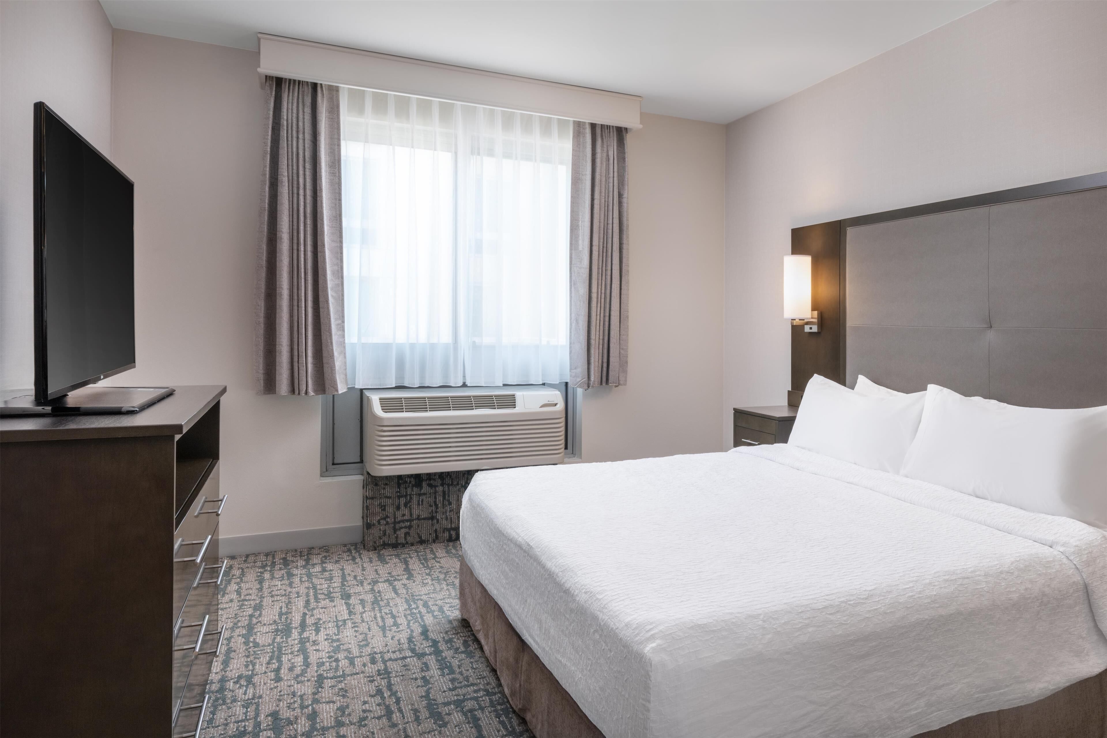 Une chambre d’hôtel dotée d’un grand lit, d’un téléviseur à écran plat, d’un système de climatisation, d’une table de chevet et d’une fenêtre avec des rideaux.