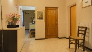 A hallway with a wooden door, a chair, and a desk with a vase of flowers. - Florence Decamerone B&B (Florence)