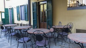 An outdoor café with round tables and chairs, a door with green shutters, and a stone floor. - Florence Decamerone B&B (Florence)
