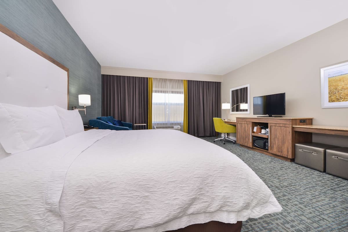 A hotel room with a large bed, a desk with a television, a chair, and a small kitchenette.
