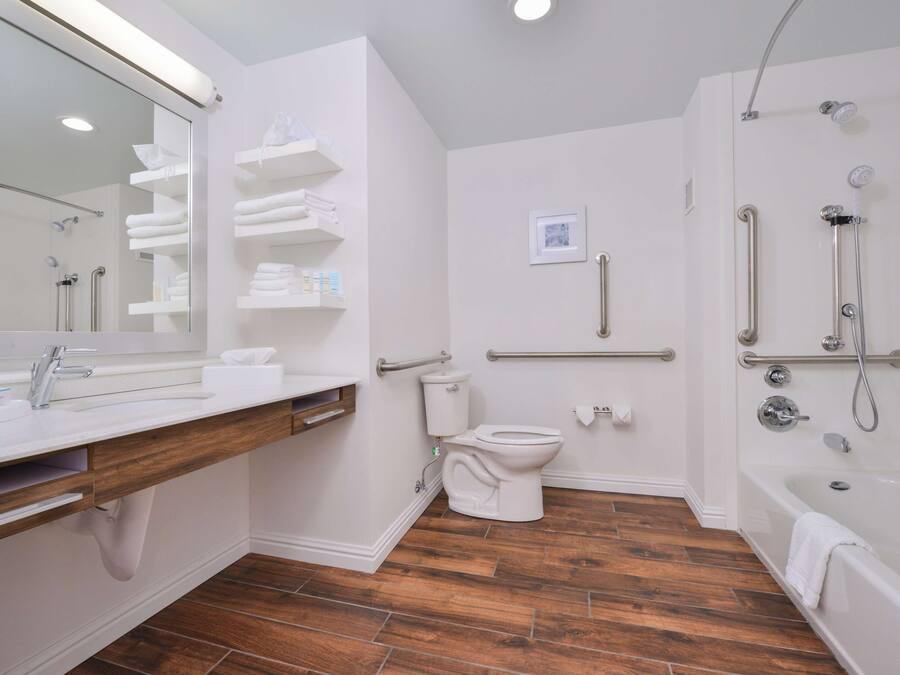 Een moderne badkamer met een houten wastafelmeubel, een toilet, een douche met grepen en een bad.