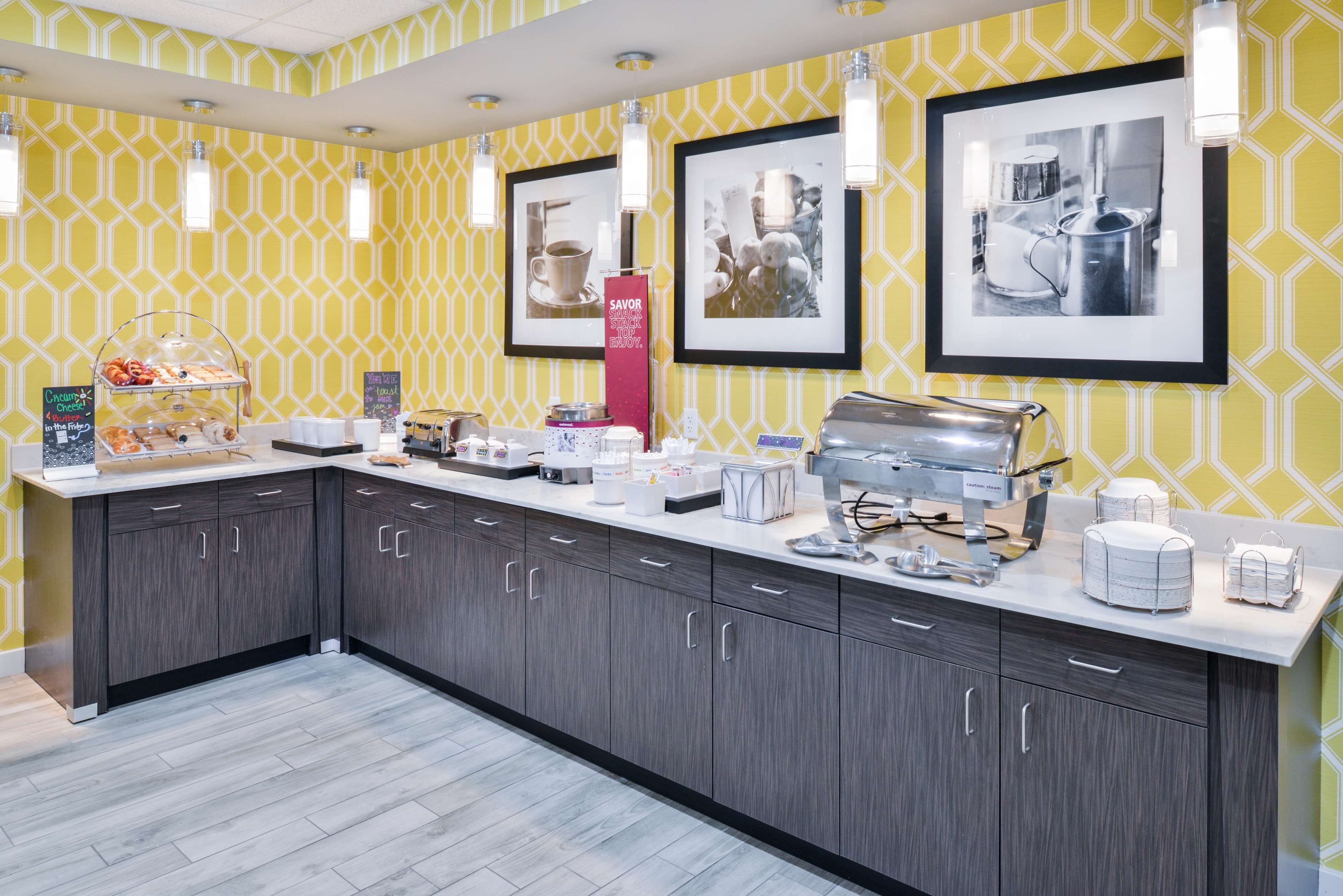 A modern kitchen with a breakfast bar, coffee machines, and a display case with pastries.