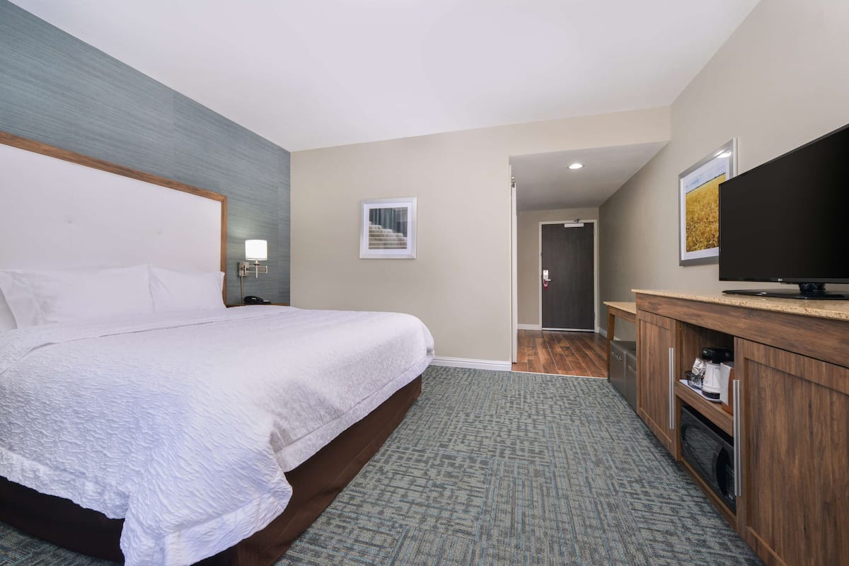 A hotel room with a large bed, a television, a wooden cabinet, and a small picture on the wall.