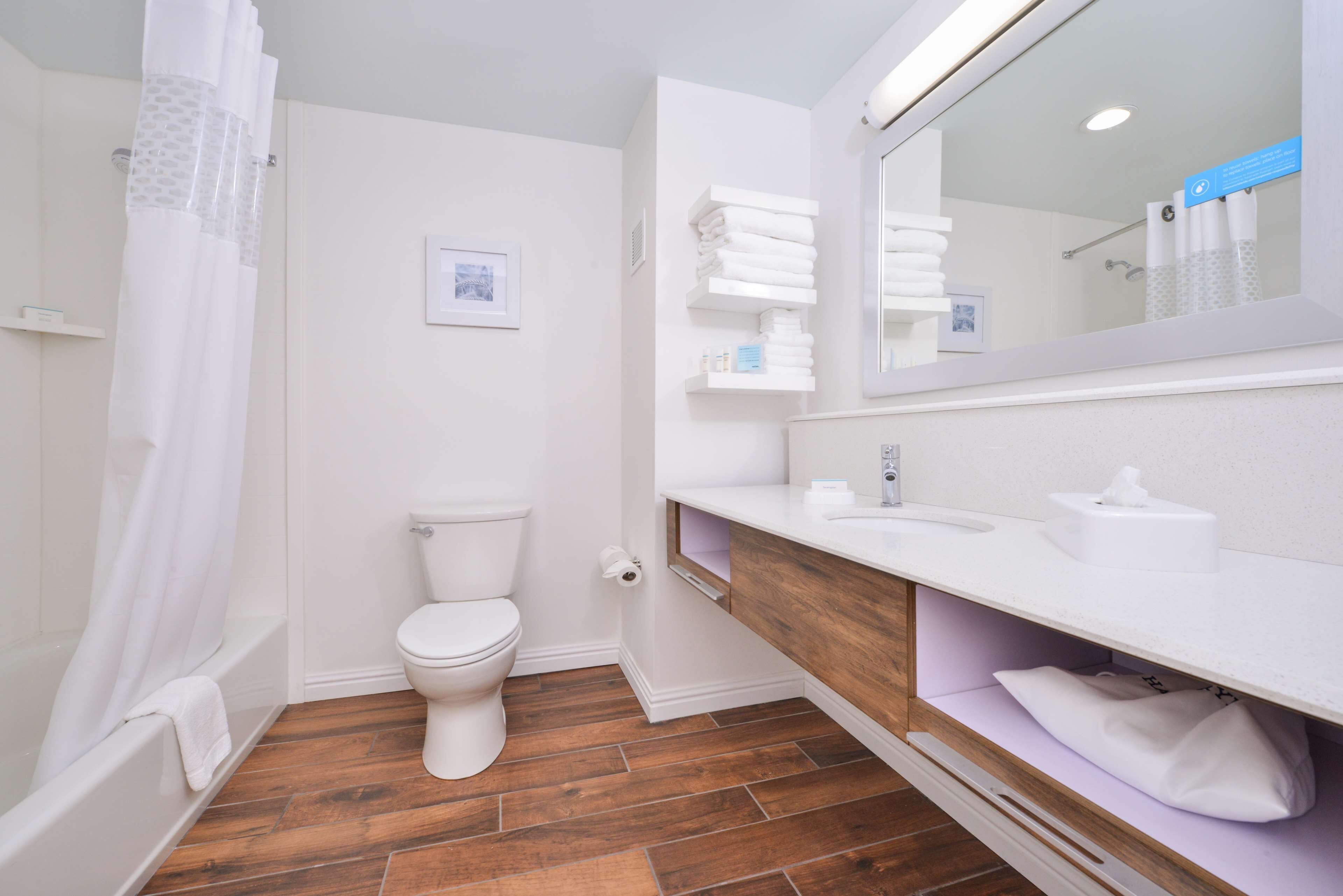 A modern bathroom with a wooden floor, white fixtures, and a large mirror.