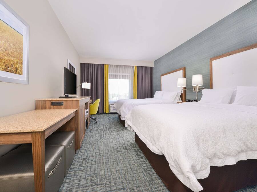 A hotel room with a bed, a desk, a television, and a window with curtains.