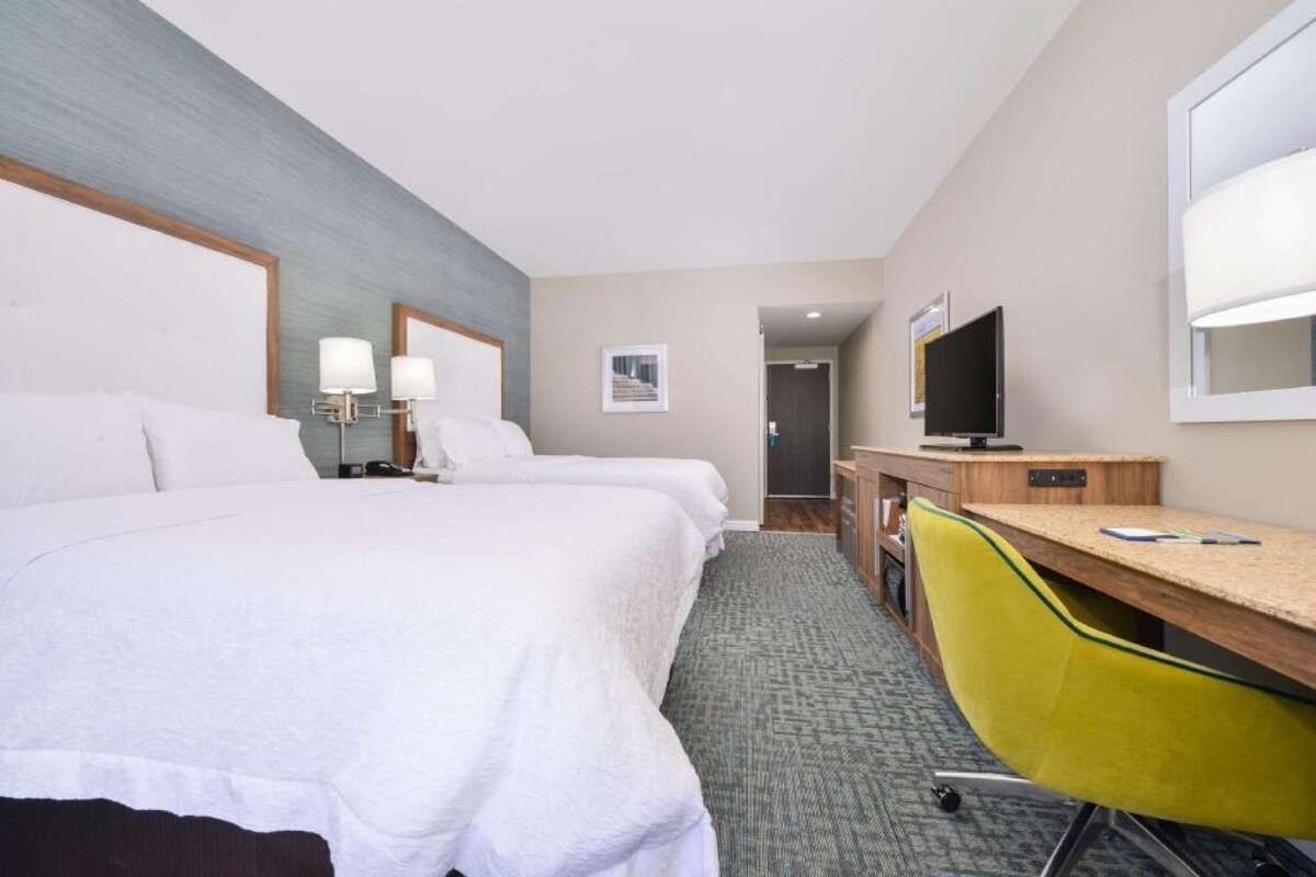 A hotel room with two beds, a desk, a chair, a television, and a mirror.