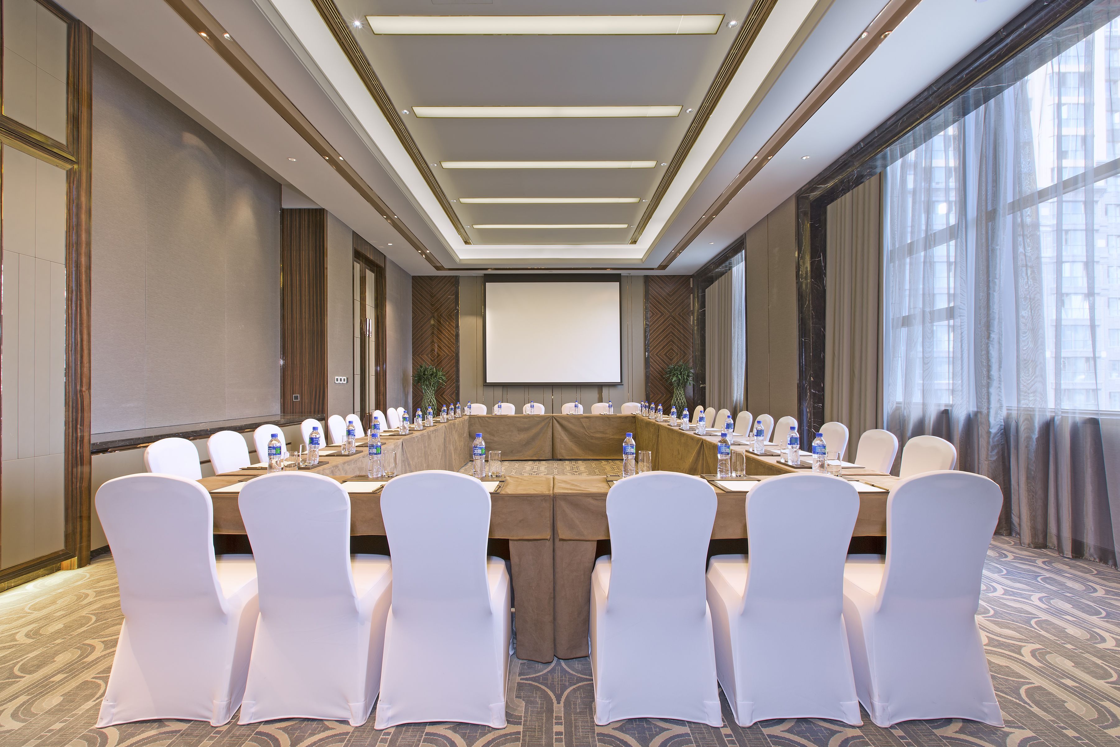 Un salón de conferencias con una larga mesa, sillas blancas y una pantalla para proyector.