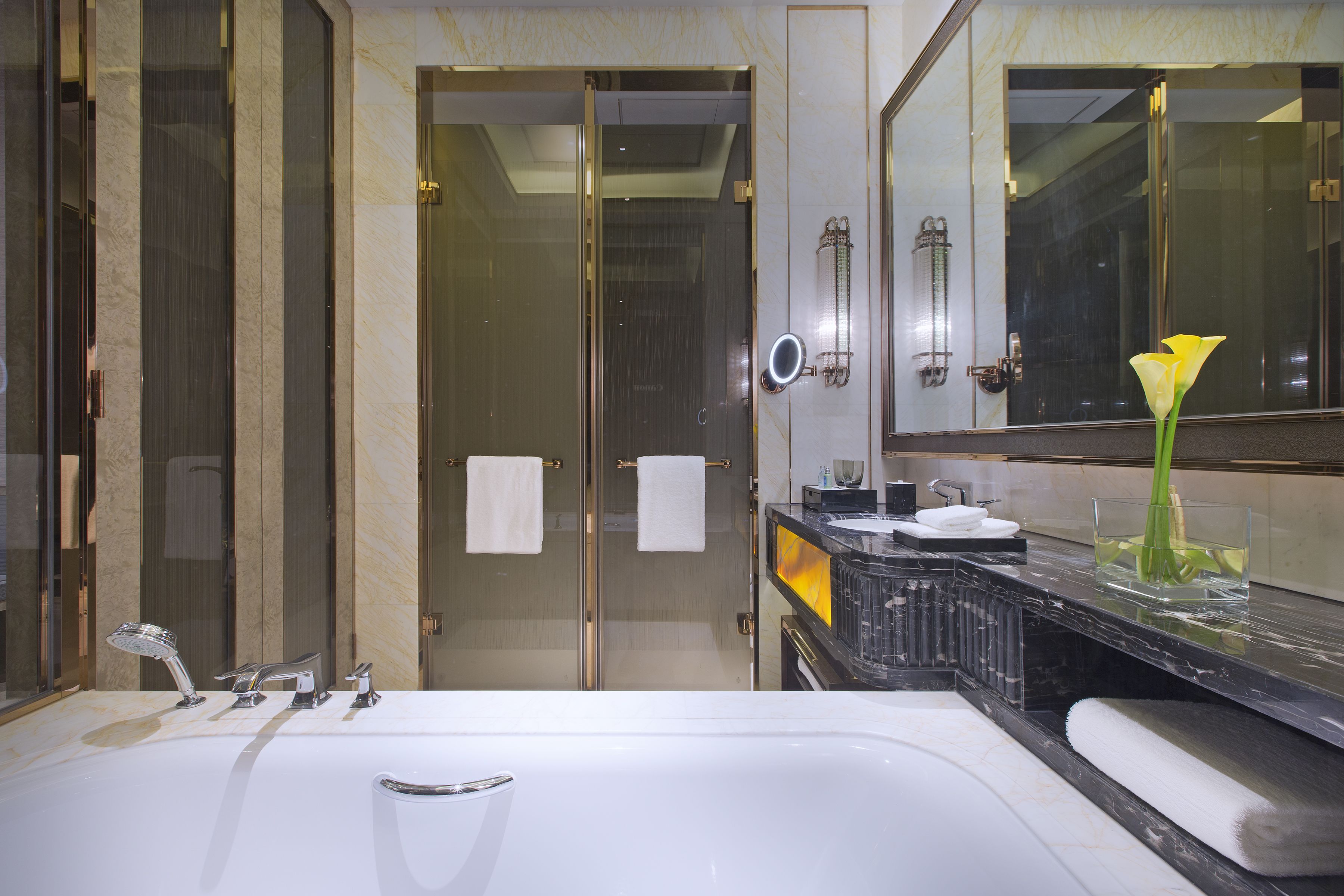 Une salle de bain moderne avec un grand lavabo, une douche en verre et un miroir agrémenté d’un vase à fleurs.