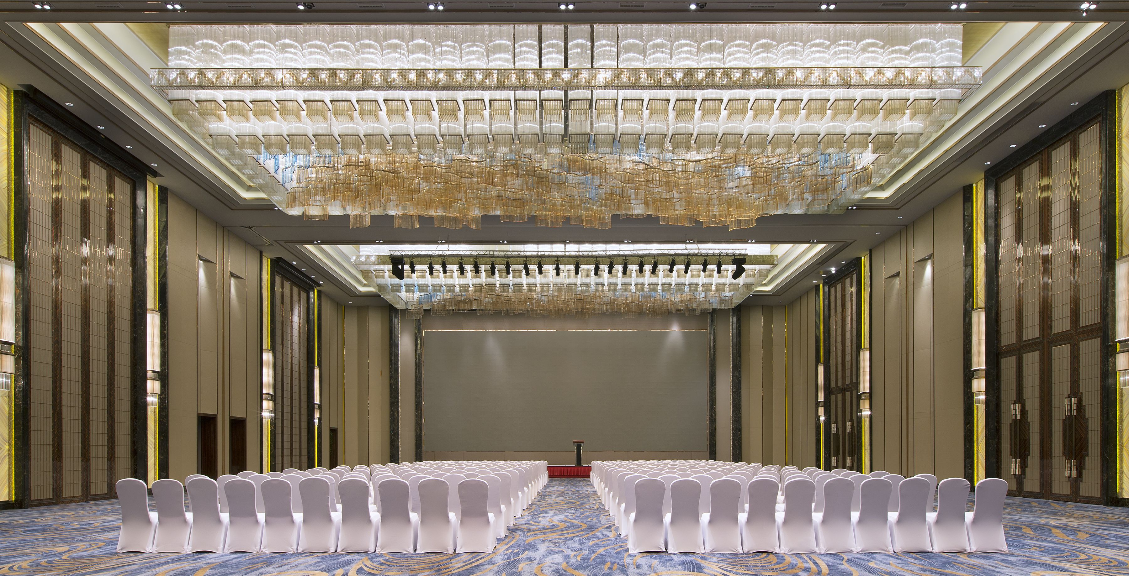 A large conference room with rows of white chairs, a podium, and a decorative ceiling.