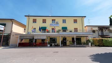 Un hotel con facciata gialla, diverse bandiere e un cartello con la scritta "Hotel Benaco".