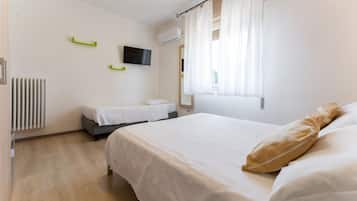 Camera d'albergo con un letto grande, un letto più piccolo, una TV a parete e una finestra con tende.